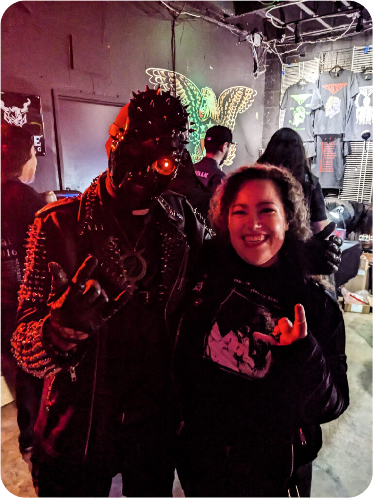 A photo of me and Mercury of the band Priest. We are both dressed in black and flashing the horns. I am clearly delighted.